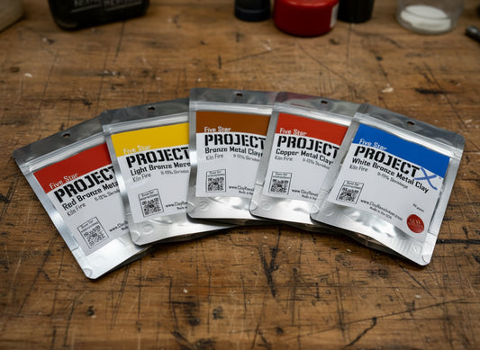Five packages of 'Project' metal clay on a wooden surface